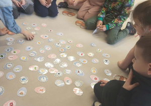 Grupa dzieci segreguje małe obrazki jajek do odpowiednich koszyczków z literkami.