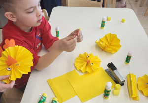 Chłopiec precyzyjnie wykleja papierowego kurczaczka z harmonijki.