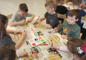Grupa dzieci przy stoliku koloruje farbami swoje prace plastyczne.