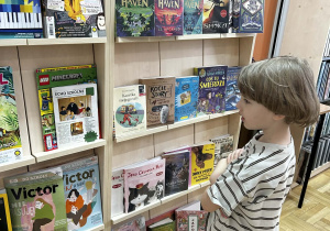 Chłopiec z zaciekawieniem przegląda kolorowe książki i czasopisma na regale w bibliotece