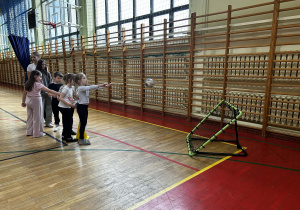 Dziewczynka oddaje rzut piłką do bramki treningowej, podczas gdy pozostali koledzy czekają w kolejce.