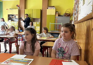 Dziewczynki siedzą w ławkach, uważnie słuchając.