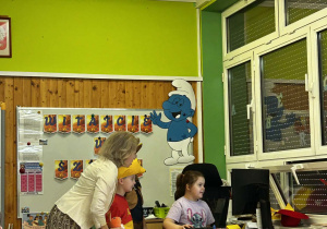 Dziewczynka pod okiem pani korzysta z komputera wykonując zadanie.