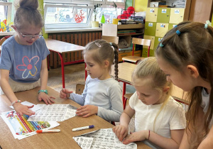 Grupa dziewczynek pracuje przy stoliku, starannie składając kartki papieru podczas zajęć manualnych.