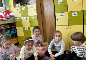 Dzieci siedzą na dywanie i biorą udział w grze zręcznościowej polegającej na „łapaniu” owadów plastikowymi łapkami.