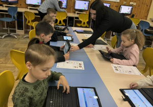 Dzieci pracują przy tabletach z podłączonymi klawiaturami, ucząc się podstaw programowania pod okiem nauczyciela