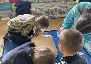 Chłopiec pod nadzorem nauczyciela ćwiczy wykonywanie wdechów ratowniczych na fantomie do resuscytacji.