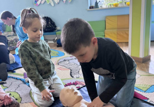 Chłopiec klęczy przy fantomie i wykonuje masaż serca.