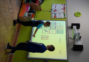 Chłopiec korzysta z nowoczesnej tablicy multimedialnej, dopasowując obrazki do pór roku: wiosny i zimy.