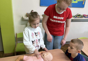 Dziewczynka pod okiem pani ćwiczy sprawdzanie funkcji życiowych na fantomie niemowlęcia.