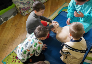 Dzieci klęczą wokół fantomu osoby dorosłej, ucząc się udrażniania dróg oddechowych i podstaw pierwszej pomocy.