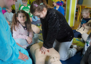 Dziewczynka z zaangażowaniem wykonuje uciski klatki piersiowej na fantomie podczas pokazu pierwszej pomocy.