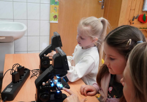 Dwie dziewczynki w skupieniu obsługują nowoczesne mikroskopy cyfrowe.