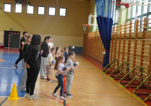 Na sali gimnastycznej dzieci trenują rzuty piłką do specjalnych bramek pod okiem nauczycieli
