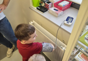 Chłopiec samodzielnie mierzy ciśnienie za pomocą aparatu naramiennego.