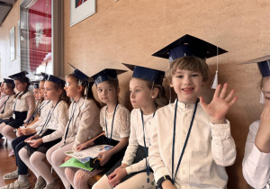 dzieci siedzą w białych koszulkach z biretami na głowie