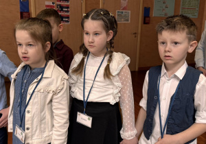 dwie dziewczynki i chłopczyk stoją patrząc i słuchając