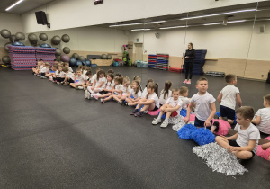 dzieci siedzą przy ścianie z luster, trzymając pompony