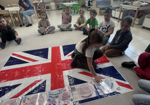 dzieci siedzą w kole i dziewczynka w środku układa kartę z informacja na fladze