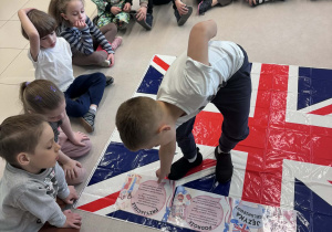 dzieci siedzą w kole, chłopiec układa kartę z informację na fladze