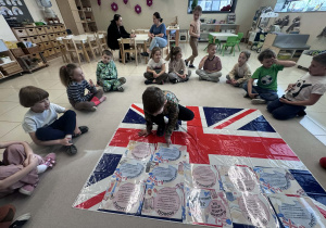 dzieci siedzą w kole, chłopiec układa kartę z informację na fladze