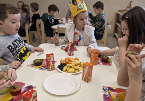 Dzieci siedzą przy stolikach na wspólnym poczęstunku