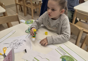 Dziewczynka skleja papierową opaskę z motywem ekologii.