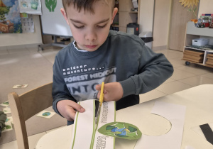 Chłopiec wycina nożyczkami papierową opaskę z napisem "Segreguj śmieci".