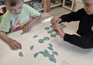 Chłopcy układają puzzle z literami na tle kuli ziemskiej.