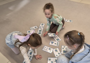 Dziewczynki grają na dywanie w ekologiczne domino z figurami geometrycznymi.