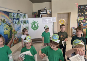 Dzieci w zielonych koszulkach bawią się gazetami.