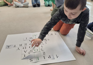 Chłopiec dopasowuje brakujące litery do papierowej krzyżówki.