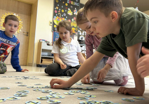 Dzieci wspólnie układają na dywanie rozsypankę literową umieszczoną na małych planetach.