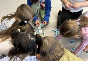 Widok z góry na grupę dzieci, które wspólnie segregują okrągłe plakietki z literami alfabetu.