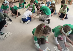 Dzieci bawią się gazetami na podłodze.