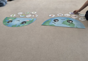 Przedszkolaki układają obrazki przy makietach smutnej i wesołej Ziemi.