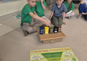 Sześciolatki uczą się segregacji do małych pojemników przy plakacie.