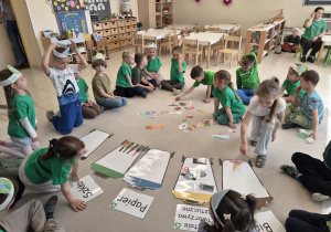 Grupa dzieci zbiera obrazki-śmieci rozsypane na podłodze.