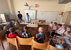 dzieci siedza w połkolu i słuchaja ucznia technikum
