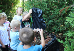 dzieci wrzucają liście do kompostownika