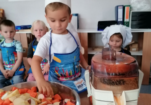 Dziecko wrzuca jabłko i marchewkę do sokowirówki